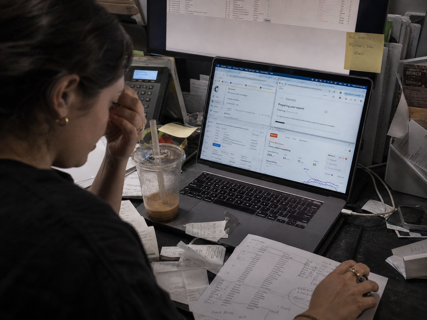 Marketing coordinator hunched over a cluttered desk juggling Mailchimp, a CSV, and a POS report on a tired laptop